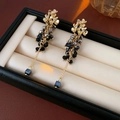 Macro detail of gold flower tassel earrings with black beads and rhinestones in a box - Silver Pin Tassel Style / Gray