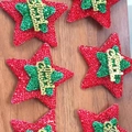 Funkelnde rote und grüne Sternornamente mit Merry Christmas Schriftzug auf Holzgrund - Weihnachtsbaum und Sterne