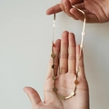 Collana a serpente dorata con ciondoli tondi piatti, tenuta da una mano su sfondo beige - Collana a 12 dischi-Oro