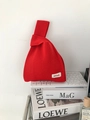 Close-up of bright red knitted knot bag showing woven texture and brand label - Red