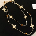 Dettaglio macro della collana a croce dorata con perle marroni e cristalli su velluto nero - Marrone oro