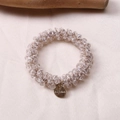 Detailed macro view of multifaceted crystal beads and MORANA metal tag on elastic hair tie - White