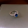 Macro shot of halo setting ring with oval blue gemstone and small zircons on silver band - Single Halo / Silver-Blue Rhombus