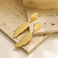 Hammered gold leaf drop earrings in titanium steel displayed on a beige stone tile - Hammered Feather / Gold