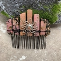 Detailed close-up of handmade crystal hair comb with sun emblem and black wire wrap - Rhodochrosite Black Wire Silver Sun