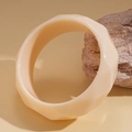 Macro detail of beige acrylic wide bangle with faceted geometric surface on natural stone - Cream White Geometric Faceted