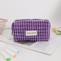 Close-up of deep purple waffle textured cosmetic bag with woven label on a desk - Purple