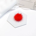 Macro view of fluffy red mink fur pompom for DIY crafts on a white pedestal - Bright Red
