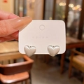 Brushed matte silver heart earrings on a minimalist white card in a warm indoor setting - E5937 Silver Brushed Heart