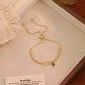 Dettaglio di un bracciale a sfere dorate regolabile con ciondolo S e occhio di Allah - Lettera S