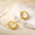 Detailopname van brede gepolijste 18K gouden oorringen op een minimalistische witte steen - Brede Minimalistische Gladde Gouden Huggie