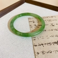 Close-up of green resin bangle with jade texture and smooth finish on beige fabric - Small / Green