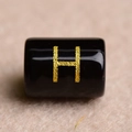Macro shot of a black cylindrical bead with a gold letter H for DIY jewelry making - Letter H