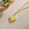 Golden necklace with a heart-shaped yellow-green pendant shown on a white fabric surface - Yellow