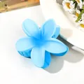 Close-up of light blue flower hair claw clip with matte finish on white ceramic plate - Gradient Blue