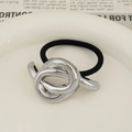 Minimalist silver twisted metal knot hair tie with black elastic band on ceramic plate - Knotted Design Silver