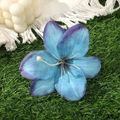 Macro view of blue and purple gradient lily hair clip on green grass background - Blue