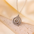 Primer plano del colgante espiral plateado sobre base de piedra con fondo de raso beige - Color Acero