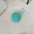 Sky blue knit yarn ball ornament with loop hanging on white plush background - Lake Blue