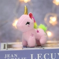 Close-up of pink plush unicorn pendant with golden horn and colorful rainbow mane - Pink