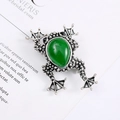 Macro shot of retro frog brooch with green teardrop stone and detailed vintage metal texture - Vintage Antique Silver Green Gem Style
