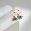 Detail von goldenen Creolen mit Türkissteinen und roten Perlen auf minimalistischem Ständer - Blau