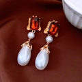 Dettaglio di orecchini vintage con perle a goccia e gemme rosse su sfondo di seta marrone - Oro/Rosso Rubino/Bianco Perla