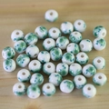 Macro shot of white ceramic beads with green floral patterns on a light wood background - No.43-Green Floral