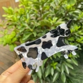 Cow pattern acrylic hair claw clip held against a lush green outdoor garden background - Cow Design - Acrylic Hair Claw