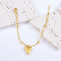 Elegante gouden slangenarmband met hartvormige hanger en kralen op een stenen basis - Armband
