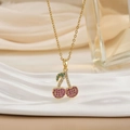 Gold cherry pendant necklace with colorful rhinestones on a white wavy display stand - Gold Pink Purple Rhinestone Cherry