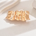 Gros plan de la pince à cheveux dorée à texture ondulée sur fond en pierre minimaliste - Doré