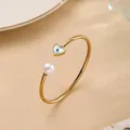 Gold open bangle featuring a pearl and heart-shaped evil eye pendant on a beige surface - Gold - Evil Eye Pearl