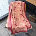 Detail of pink knitted scarf with white cherry patterns and fringe tassels on a wooden chair - Pink