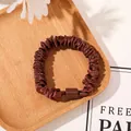 Detail of a dark brown pleated satin hair scrunchie on a wooden tray with floral accents - Satin Solid Bronze