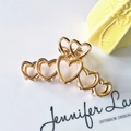 Detail of golden heart-shaped metal hair claw clip with hollow design and glossy finish - Heart