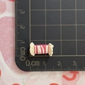 Makro-Detail von Miniatur 1,2 cm rosa Harz Bonbon Zubehör auf einer Metrikmatte - Enoki-Pilz-Fleischrolle