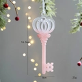 Pink gradient key Christmas ornament with white ribbon and size details on pine branch - Key