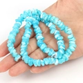 Close-up of irregular blue and white shell beads bracelet held by hand on white background - Irregular Blue