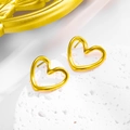 Close-up of golden hollow twisted heart stud earrings on a textured white stone pedestal - Hollow Heart Studs / Gold Earrings