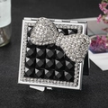 Square silver folding makeup mirror with luxury rhinestone bow on faceted black surface - Black