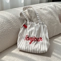 Detailaufnahme der gestreiften Canvas-Tasche mit roter Bonjour-Stickerei auf dem Sofa - Weiß
