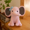 Plush pink baby elephant toy with a blue bow tie sitting in a cozy home setting - Pink/Blue Bow