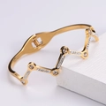 Dettaglio del bracciale a onde placcato oro 18k con zirconi bianchi su un supporto di pietra - Oro