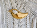 Detail of wooden bird brooch with pin fastening on a grey knitted sweater fabric - Bird