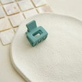 Close-up of a matte teal square hair claw clip on a textured ceramic dish - Cyan