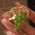 Designer vintage grape brooch with golden leaves and green beads shown on a book page - Green
