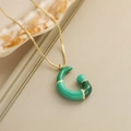 Dettaglio del ciondolo a forma di C in bambù verde su una collana a catena dorata - Lettera G