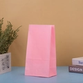 Close-up of a plain pink kraft paper gift bag on a blue surface with minimalist decor - Pink