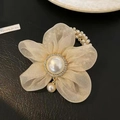Close-up of champagne organza flower hair tie with pearl center and rhinestone details - Beige